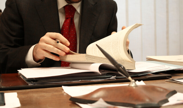 Expert Legal Review: Kash Legal Group's Approach A lawyer in a suit and red tie examines legal documents at a desk
